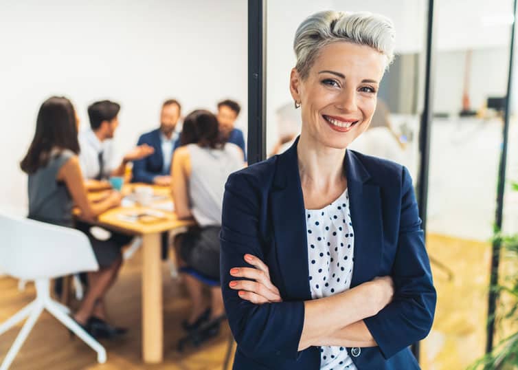 Smiling, professionally dressed broker-in-charge with a team of real estate brokers sitting at a conference table behind her