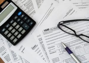 Tax forms spread out on table with calculator, pen, and eyeglasses