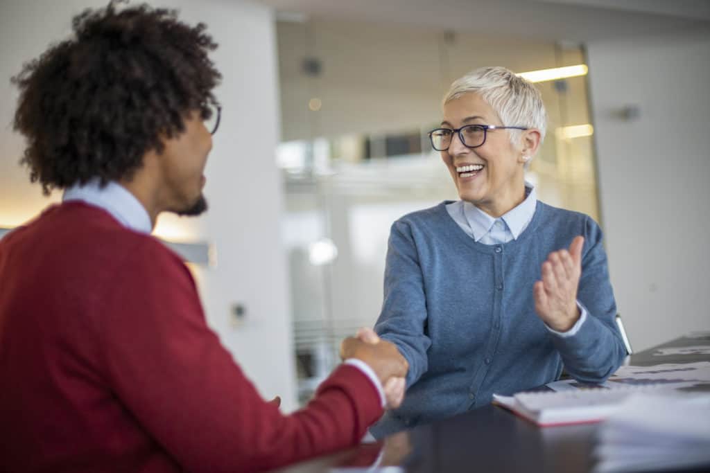 Mature gray haired woman and young businessman handshaking and greeting at meeting in office