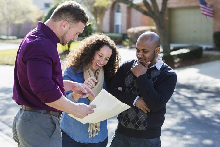 Broker showing document to smiling North Carolina real estate clients in residential neighborhood