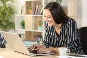 Happy woman typing on laptop, taking online real estate classes from home