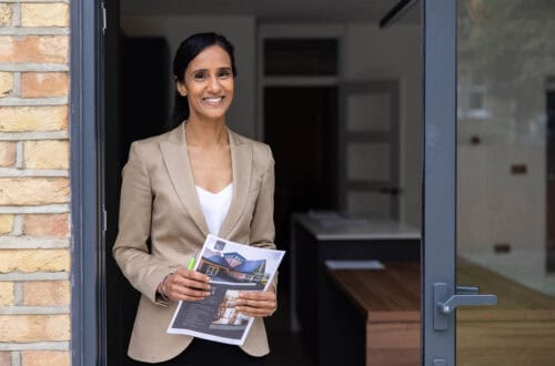Real estate agent opening the door of a house and holding brochures