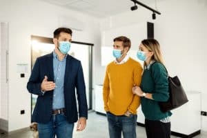 Young couple and male real estate broker wearing face masks while looking a new home