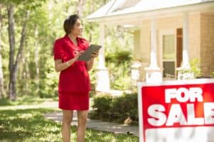 Young North Carolina real estate broker with home for sale uses digital tablet while standing in yard
