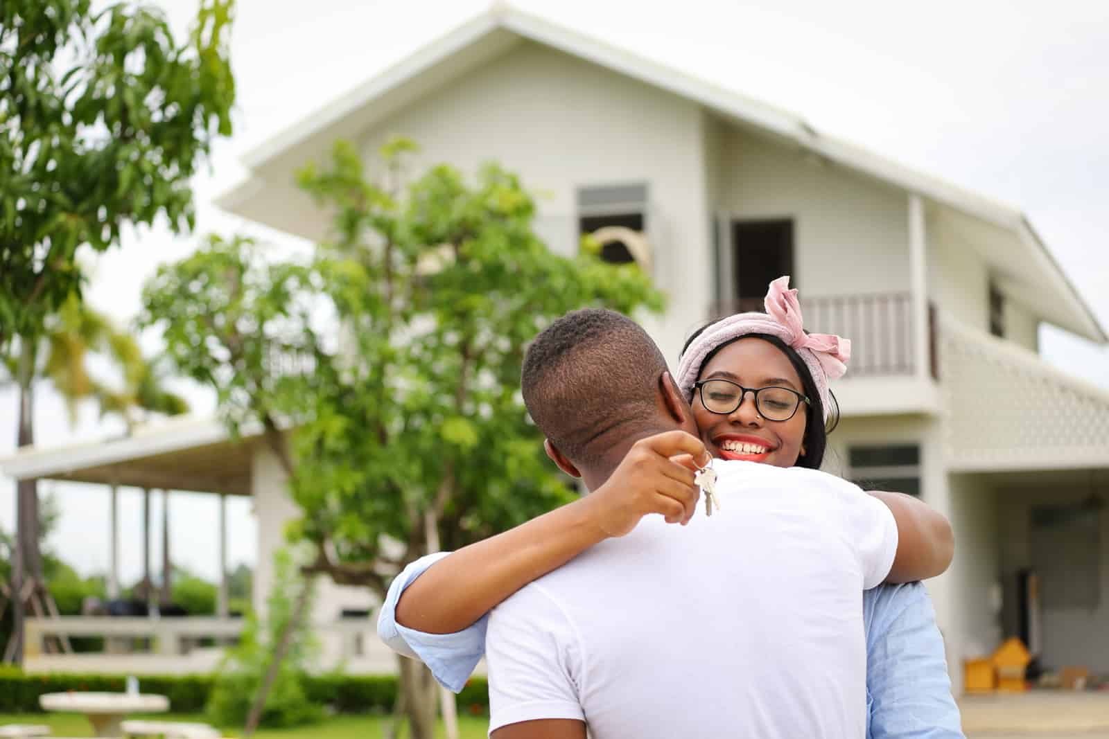 African American Generation Z homebuyers, young married couple hugging in front of the house they just bought