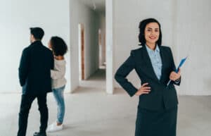 Real estate agent smiling to the camera, showing a home to a young couple