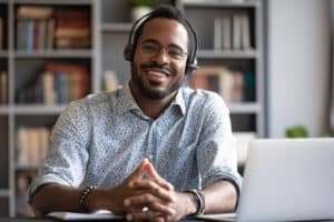 African man wearing headphones sits at desk smiling, completing professional development course online