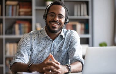 African man wearing headphones sits at desk smiling, completing professional development course online