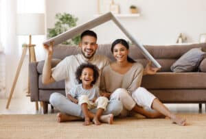 North Carolina homebuyers, parents with child smiling and roof mockup over heads while sitting on floor in cozy living room, relocation concept