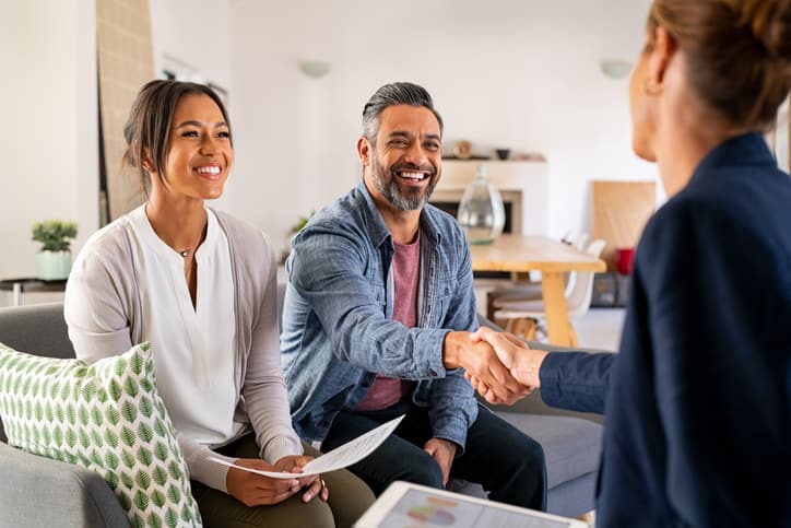 Happy smiling couple greeting North Carolina real estate broker with handshake at home.