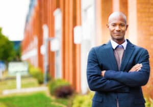 Confident real estate professional smiling, arms crossed, with real estate background