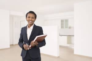 Smiling young real estate professional assesses value of vacant residential property, dressed in professional clothing to reflect her personal real estate brand.