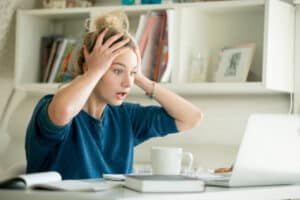 Young real estate professional working on laptop, grabbing her head, frustrated at what she sees on screen. Real estate technology frustrations concept.