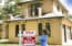 young adult realtor standing beside her for sale sign in front yard of home. She adds the SOLD sign and wears a blue top and jeans.